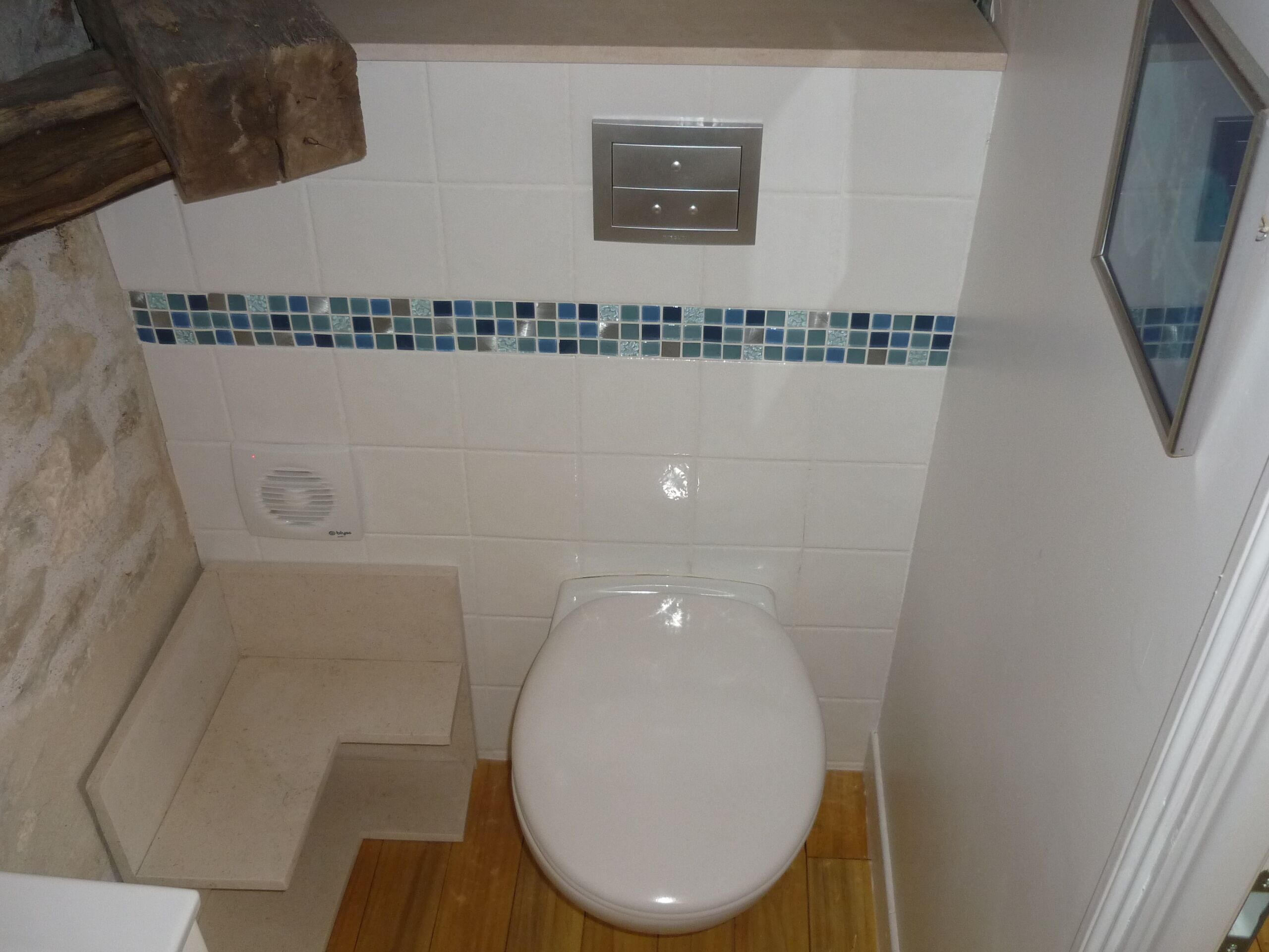 Une salle de bain avec des toilettes blanches, un mur recouvert de carreaux bleus et un plancher en bois.