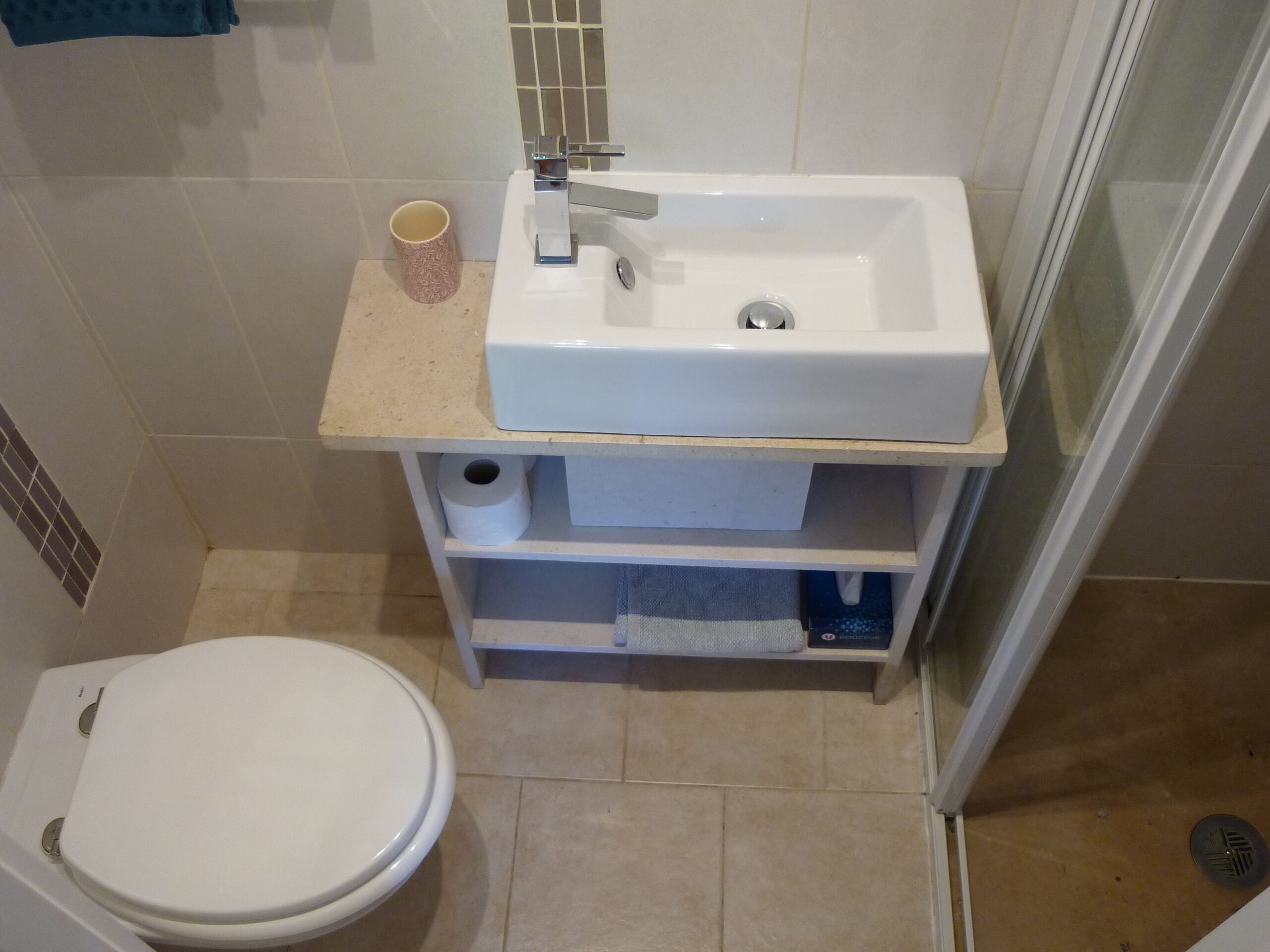 Un bagno piccolo con il water, un lavandino e una tazza sul ripiano.