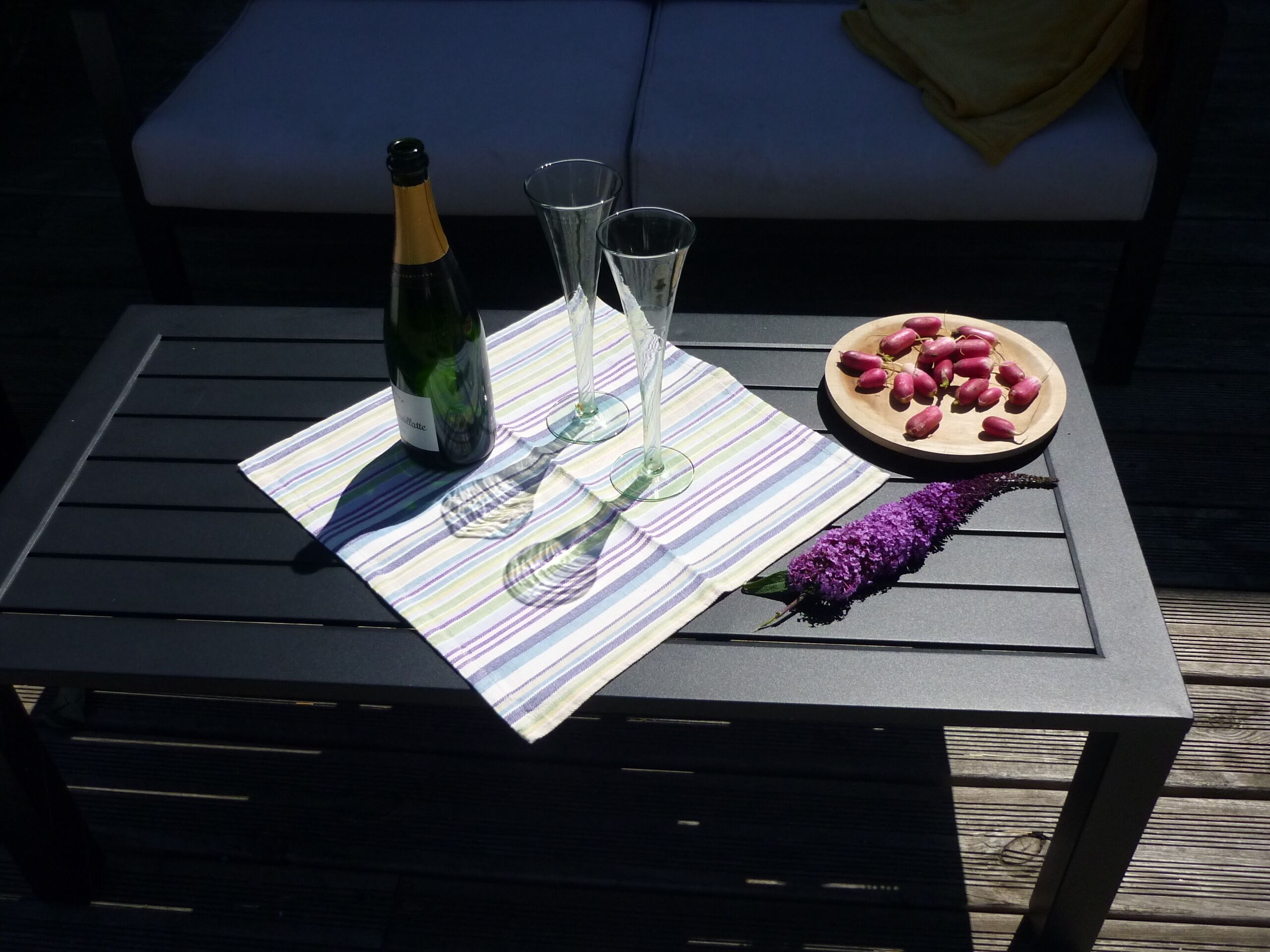 A table with a bottle of champagne, two glasses, and a plate of grapes on a striped tablecloth.