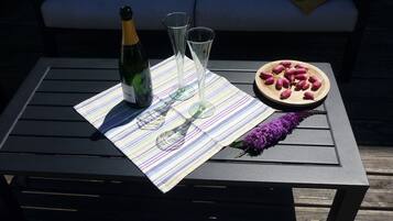 A table with a bottle of champagne, two glasses, and a plate of grapes on a striped tablecloth.