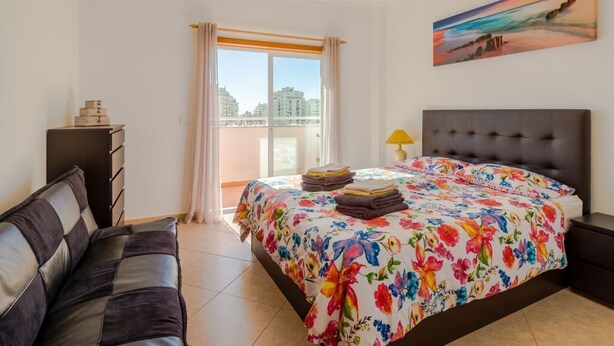 A bedroom with a bed, a sofa, a nightstand, a lamp, and a painting on the wall.
