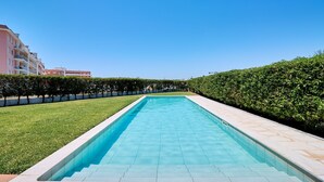 A rectangular swimming pool with clear blue water, surrounded by a well-maintained lawn and a hedge.