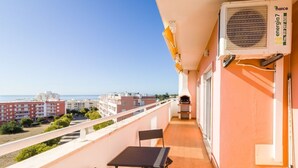 A balcony with a table and chairs, a grill, and an air conditioning unit.