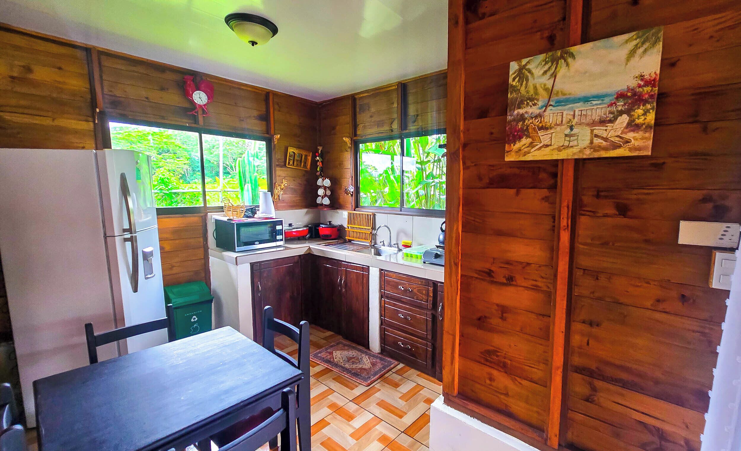 A compact kitchen with wooden walls, a dining table, and a view of greenery through the windows.