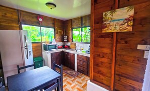Une cuisine compacte aux murs en bois, avec une table à manger et une vue sur la verdure par les fenêtres.