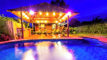 A poolside area with a covered seating area, a pool, and a stone wall.