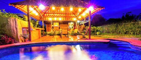 Un espace aménagé au bord de la piscine, comprenant un coin salon couvert, une piscine et un mur en pierre.
