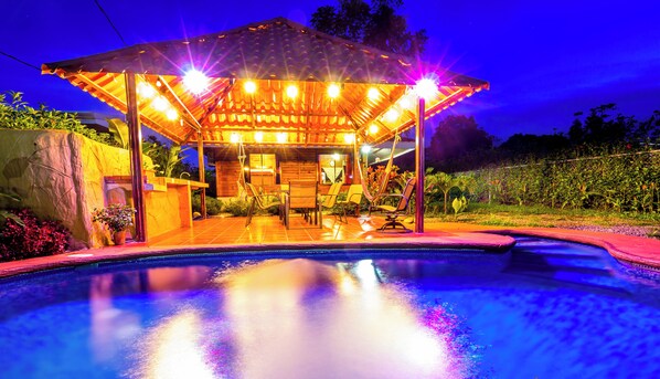 A poolside area with a covered seating area, a pool, and a stone wall.