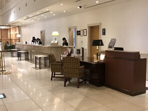 Un espace d’accueil d’hôtel avec un comptoir, des chaises et quelques personnes.