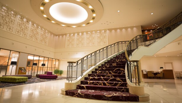 A grand lobby with a central staircase, a reception desk, and a seating area. - Hotel Grand Hills Shizuoka (Shizuoka)