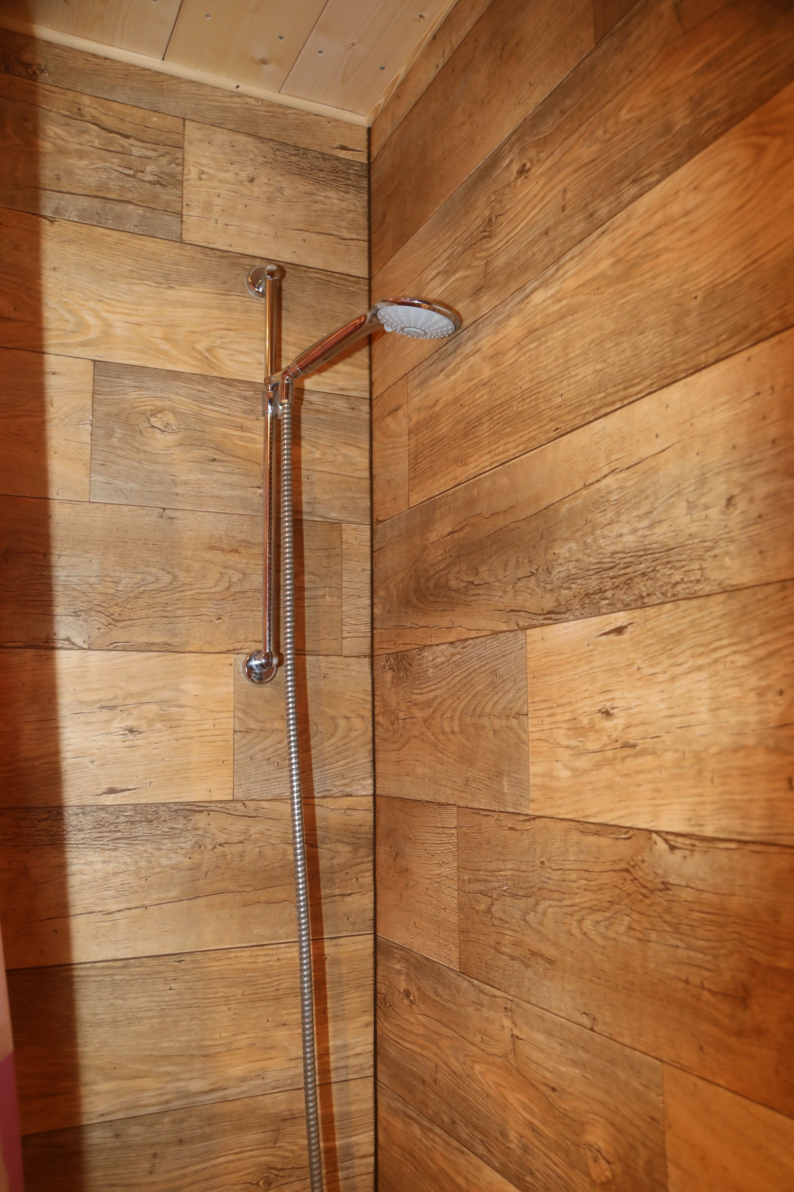 A shower with a metal hose and showerhead against a wooden wall.