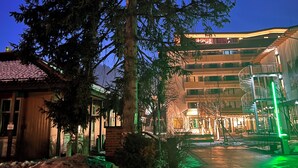 A hotel with a large tree in the foreground, a building with multiple floors, and a green-lit staircase. - Hut magic meets 5* indulgence | Lenggries on the Isar (Lenggries)