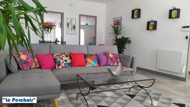 A modern living room with a grey sectional sofa, colorful cushions, a glass coffee table, and a geometric patterned rug. - Appt T2 - : 3 stars *** : near beach, îles Madame, ile d'Aix (Saint Nazaire sur charente)
