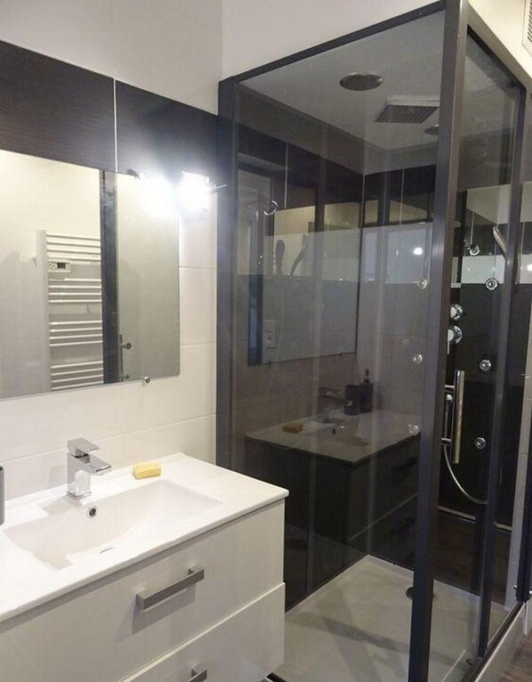 A modern bathroom with a glass-enclosed shower, a white vanity with a mirror, and a sink. - 2-room apartment: 3-star rating: Air-conditioned, near: the beach, the Madame Islands, and the Île d'Aix (Saint Nazaire sur charente)