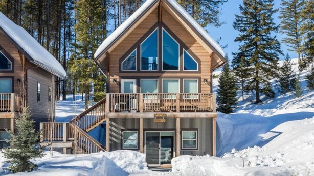 Een tweelaags lodge met balkon en een stoel van een skilift.
