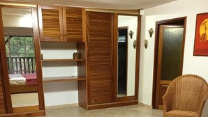 Een slaapkamer met een bed, een houten garderobe, een rieten stoel en een deur naar een balkon.