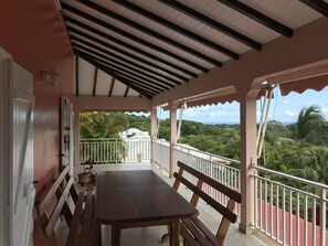 A covered outdoor area with a table and benches, overlooking a lush landscape. - Large family villa La Colombine (SAINTE-ANNE)