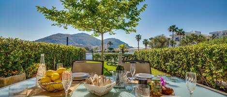 An outdoor dining table set with plates, glasses, and a basket of bread, overlooking a scenic view with mountains and a pool.