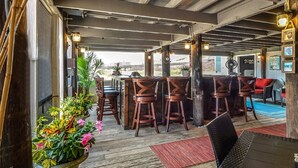 Un espacio al aire libre con una terraza, taburetes de madera, una mesa de comedor y plantas en macetas.
