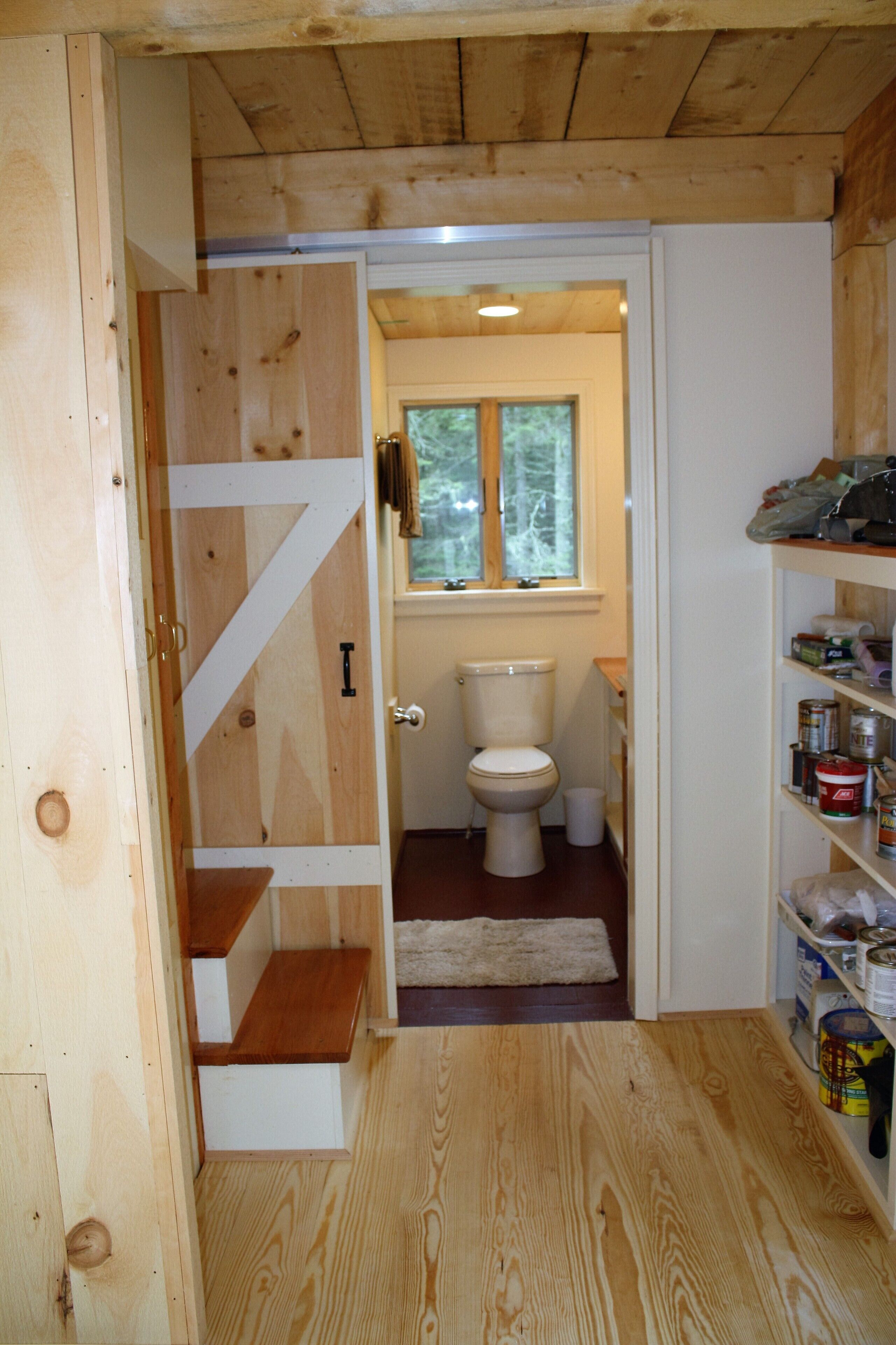 A wooden interior with a white toilet, a window, and a shelf with various items.
