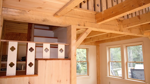 Un interior de madera con zona de dormir en un altillo, estanterías empotradas y ventanas amplias.