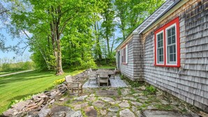 Um pátio de pedra com móveis de exterior, um deck de madeira e uma casa com detalhes vermelhos.