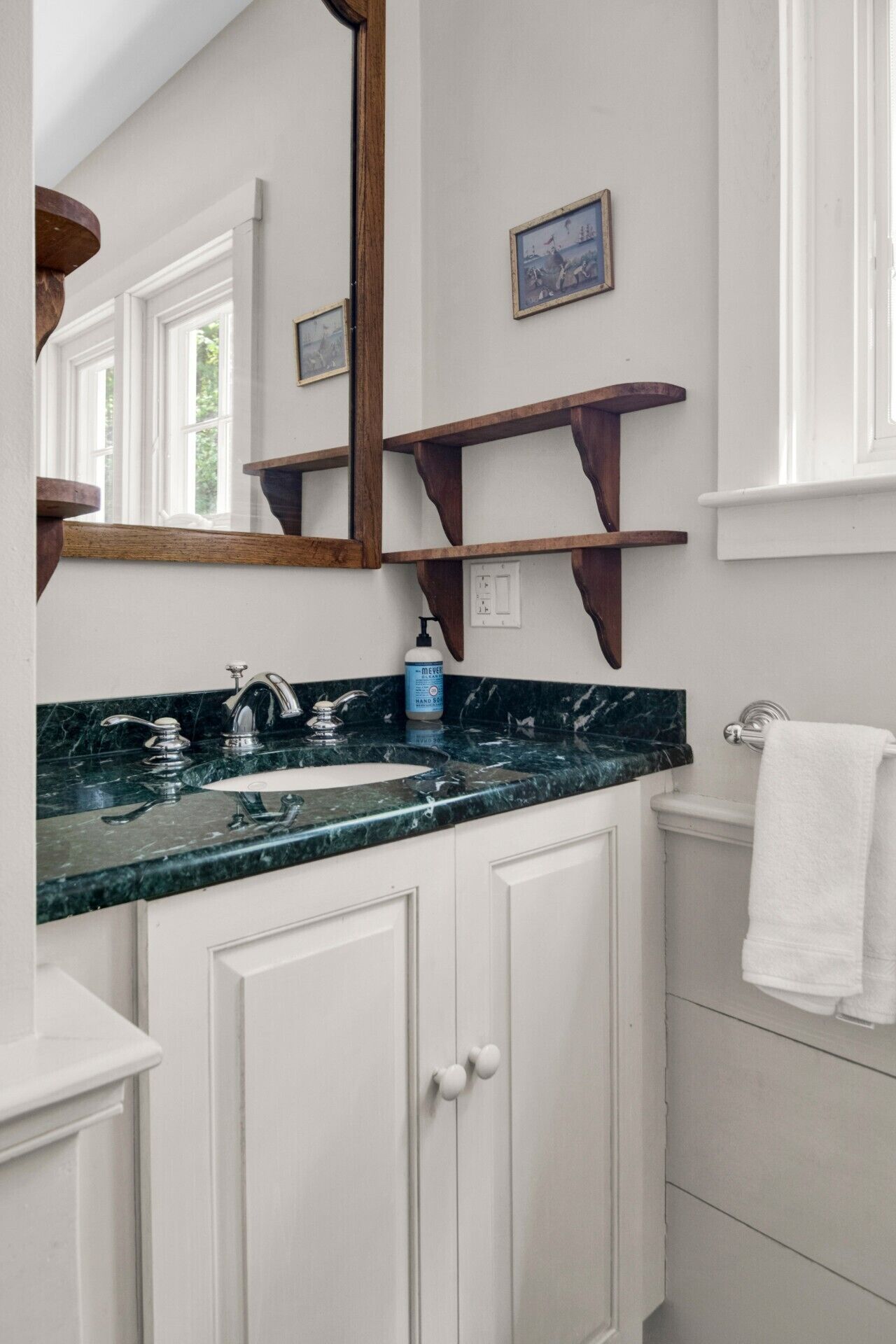 Un bagno con un piano d'appoggio in marmo, un lavandino, uno specchio, mensole in legno e un water.
