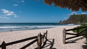 A beach with a wooden fence and a thatched roof structure.