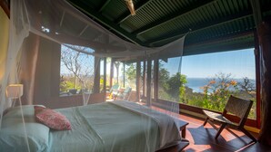A bedroom with a bed, a chair, and a view of the ocean.