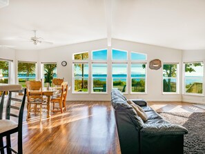 A spacious living room with a large window overlooking a scenic view, a dining area with wooden furniture, and a ceiling fan. - Water front, private beach,  King bed, Jacuzzi tub in master bedroom BBH8242 (Birch Bay)