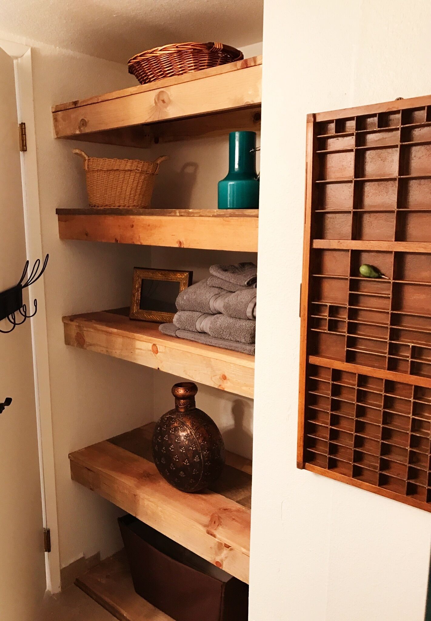 A wooden shelf unit with baskets, towels, and a vase.
