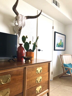 A wooden dresser with brass handles, a cactus plant, a vase, and a skull with horns on top.