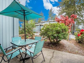 Relax in a serene patio setting surrounded by lush greenery and a vibrant flowering tree.