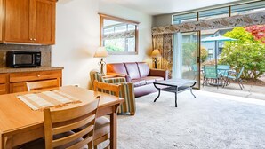 A cozy living room with a wooden dining table, a sofa, and a coffee table. There is a kitchen area with wooden cabinets and a microwave. - JL 305: Peaceful yet centrally located 2 bedroom, in the heart of Birch Bay. (Birch Bay)