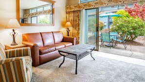 A living room with a brown leather sofa, striped armchair, and a small table. There is a large mirror on the wall and a sliding glass door leading to an outdoor area with a table and chairs. - JL 305: Peaceful yet centrally located 2 bedroom, in the heart of Birch Bay. (Birch Bay)