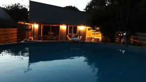 Una piscina con un porche cubierto, una mesa y sillas.