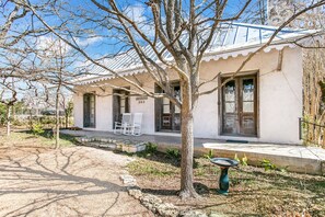 Un edificio con fachada blanca, un porche cubierto con dos mecedoras y una puerta con la etiqueta '303'.