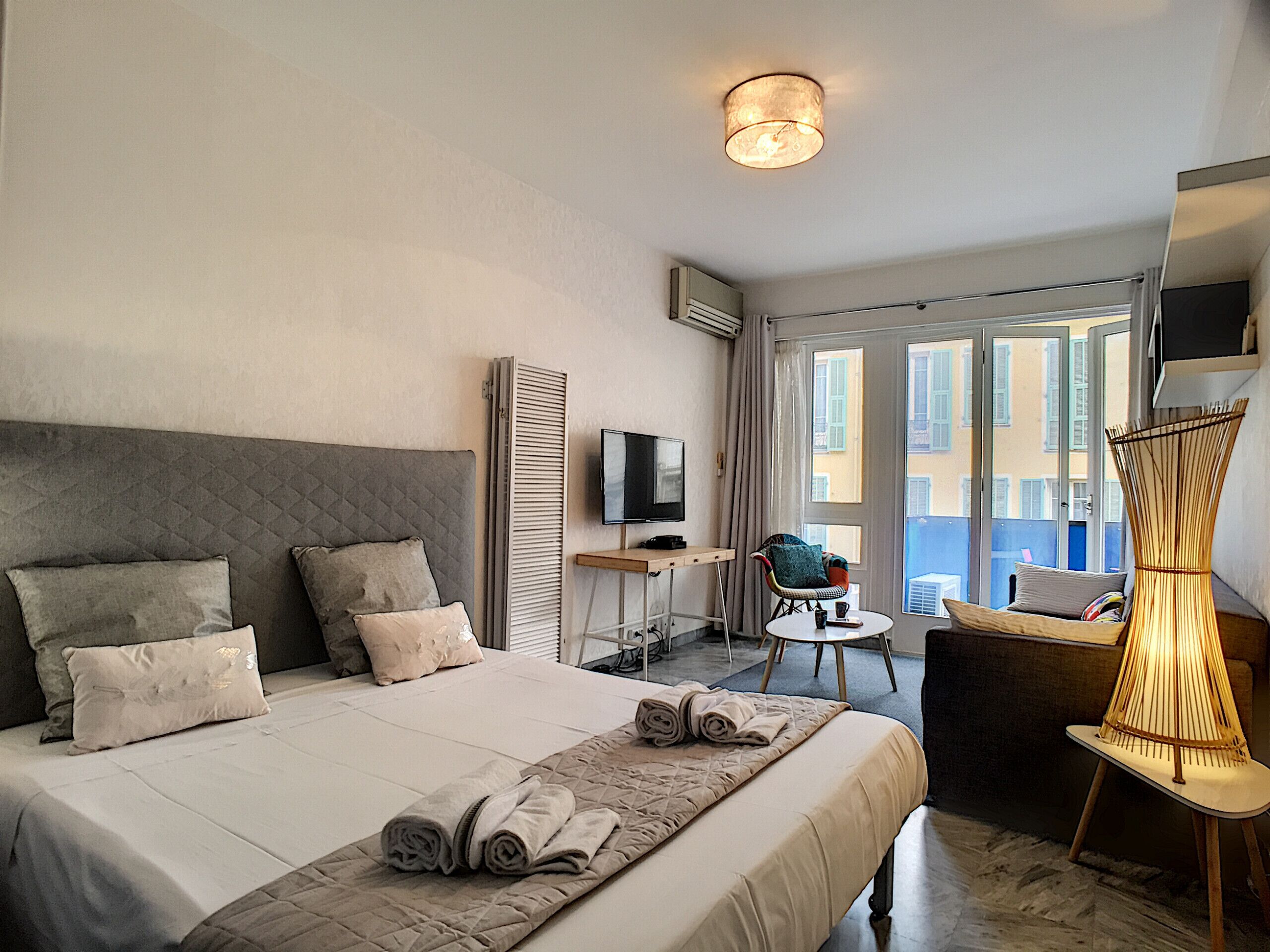A hotel room with a bed, a TV, a desk, a chair, and a balcony with a view.