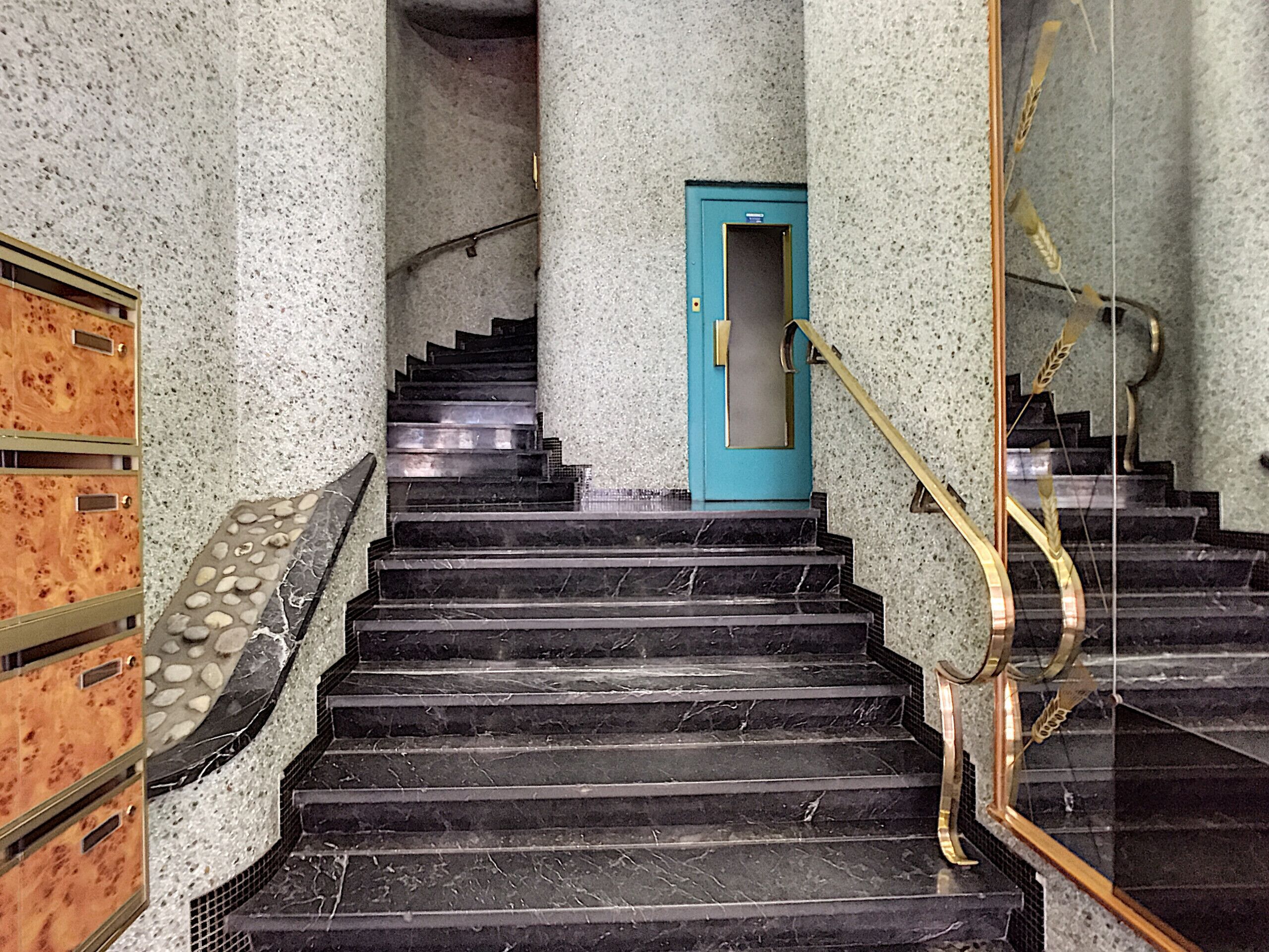 A staircase with black marble steps, a blue door, and a golden handrail.