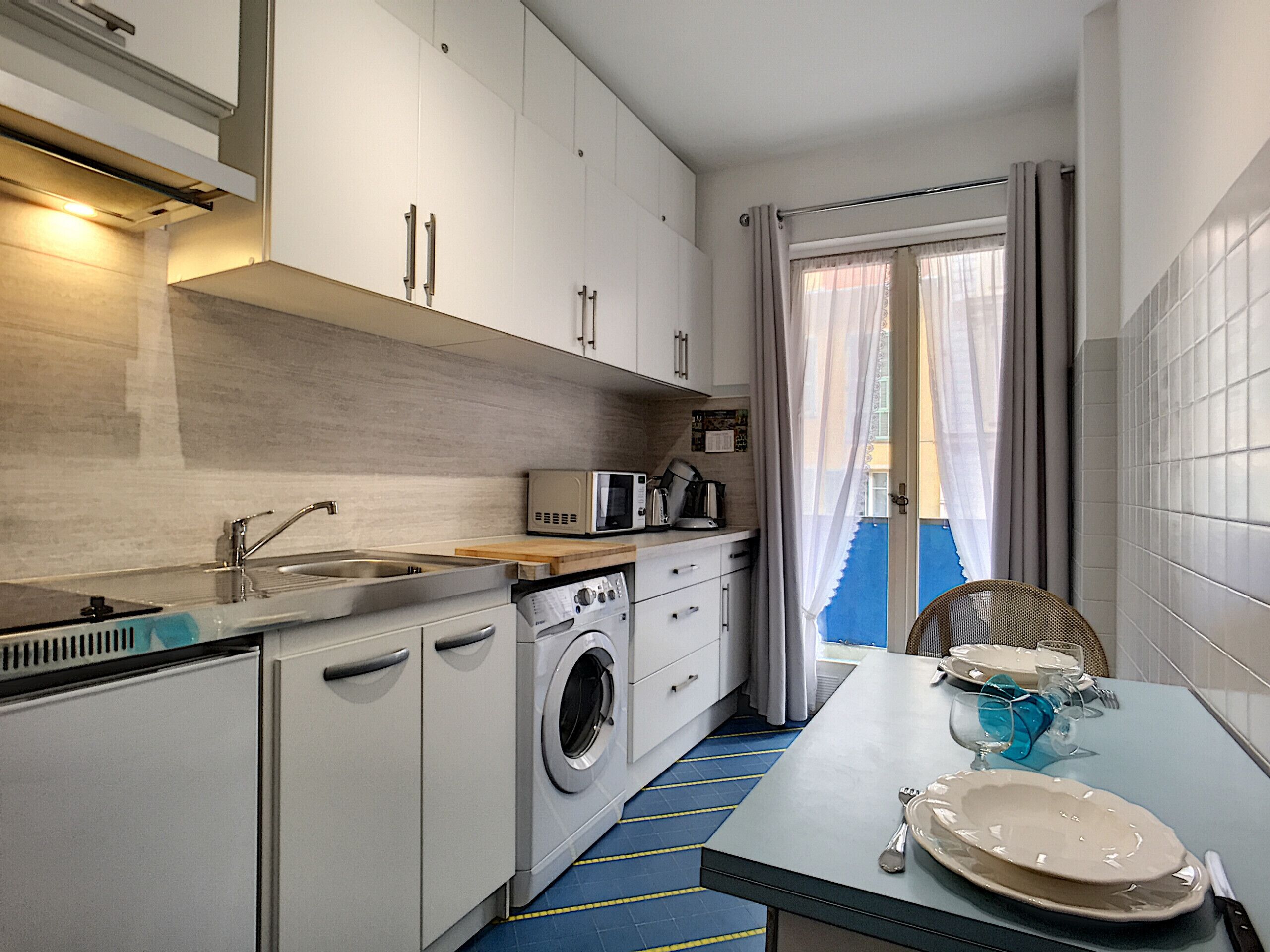 Een kleine keuken met een wasmachine, een magnetron en een spoelbak.