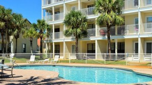 Un hotel de varios pisos con piscina, palmeras y un área de terraza cercada.