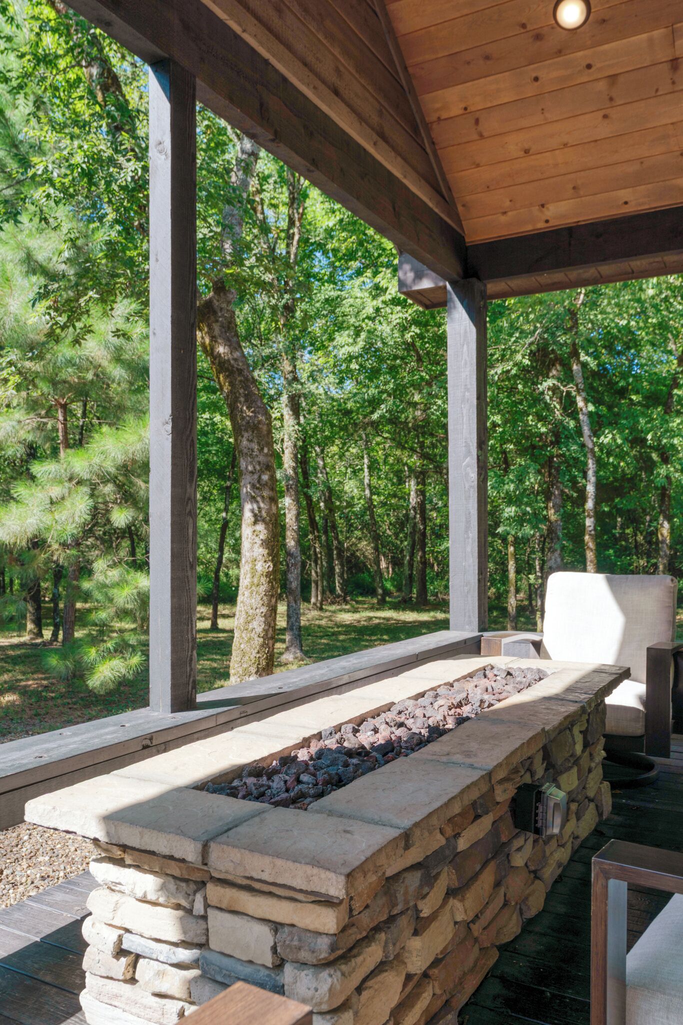 Patio esterno con focolare in pietra, travi in legno e vista su una zona boschiva.