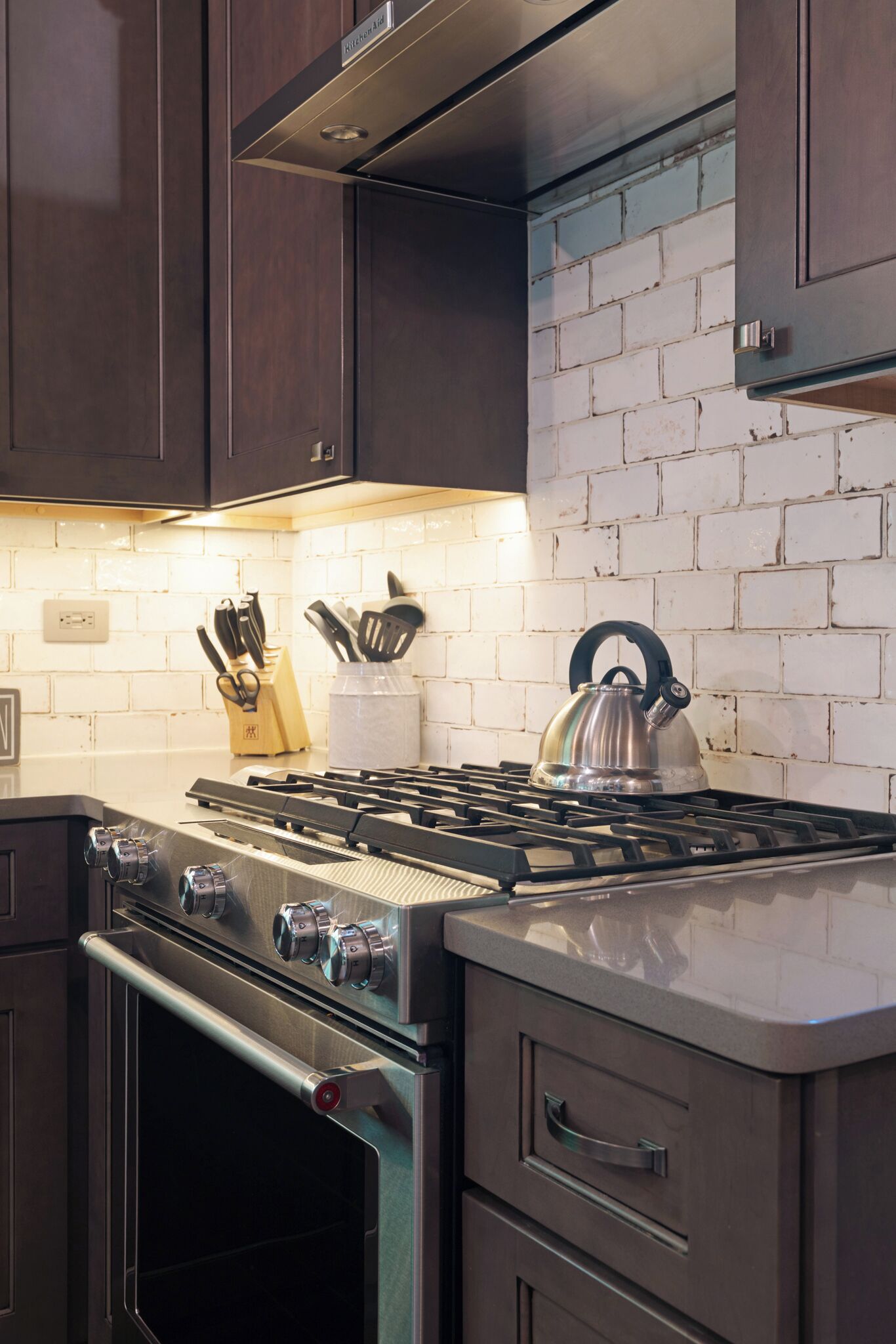 A kitchen with dark wooden cabinets, a gas stove, an oven, and a white brick backsplash.