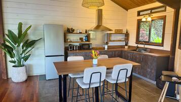 Una cocina moderna con una mesa de comedor de madera, taburetes de bar, microondas integrado y una lámpara colgante.