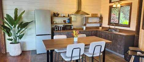Una cocina moderna con una mesa de comedor de madera, taburetes de bar, microondas integrado y una lámpara colgante.