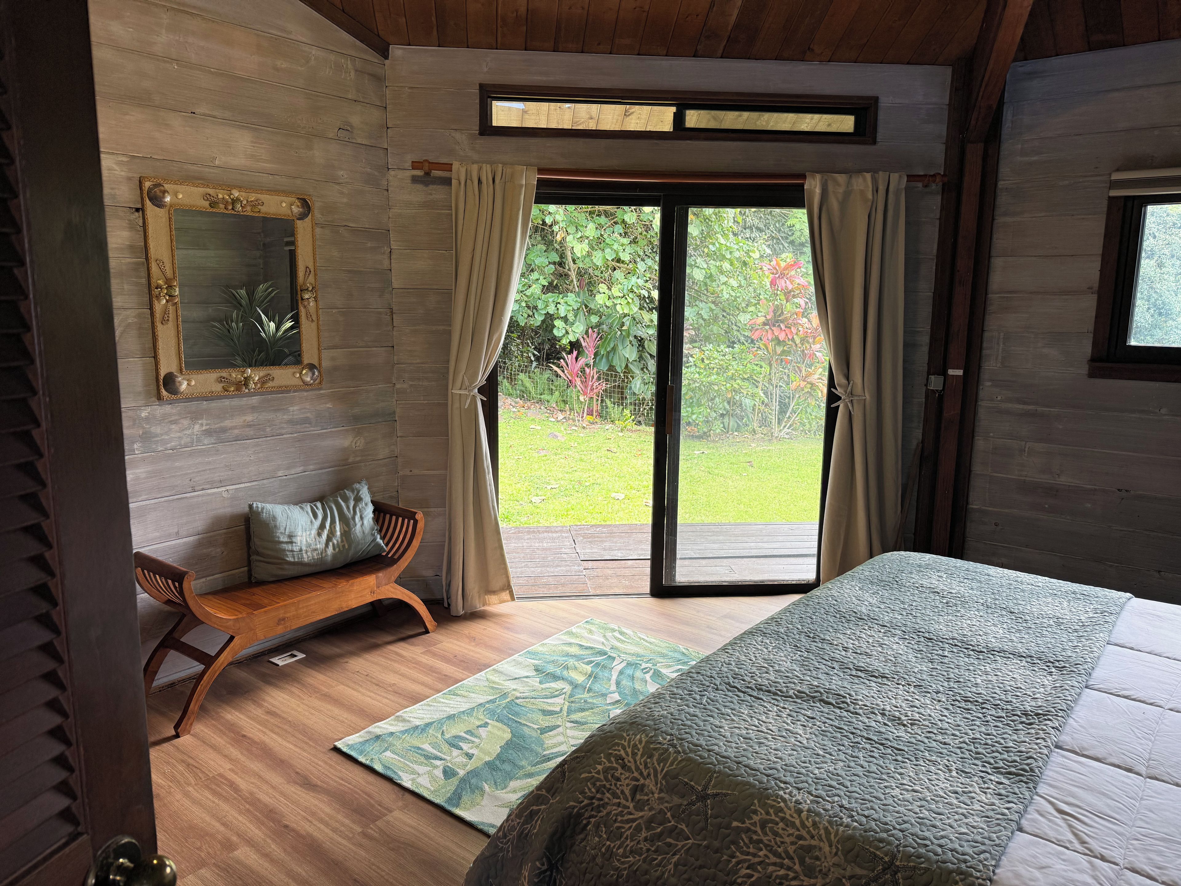 Une chambre à coucher avec un lit, un banc en bois, un miroir et une vue sur un jardin, accessible par une porte coulissante.