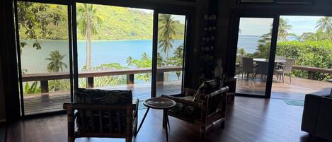 Una habitación amplia con ventanas grandes, piso de madera y vistas a un lago y colinas.