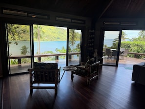 A spacious room with large windows, wooden flooring, and a view of a lake and hills.