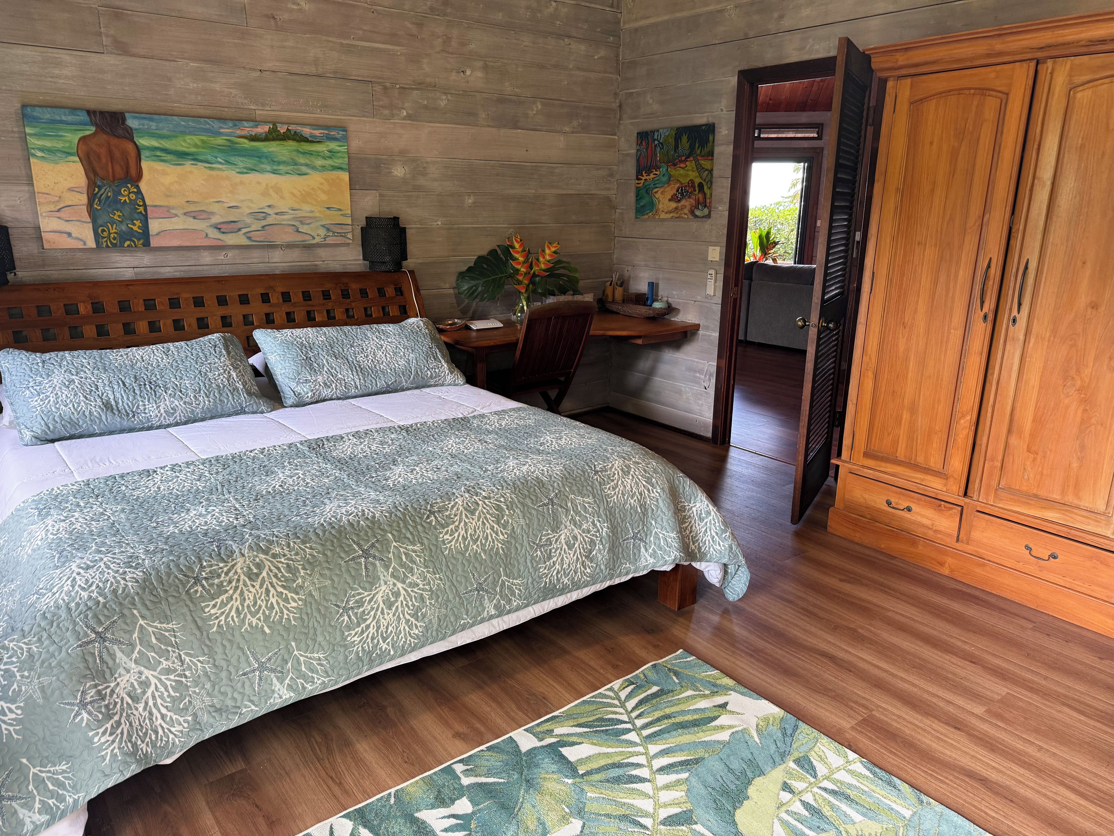 Une chambre à coucher comprenant un lit, une tête de lit en bois, une table de chevet, un bureau, une armoire et deux tableaux accrochés au mur.