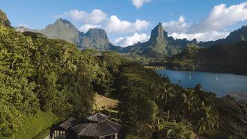 Ein tropisches Resort mit einem pavillonartigen Gebäude, umgeben von üppiger Vegetation und Blick auf einen See mit Segelbooten.